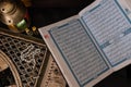 Closeup of open Quran book with rosary beads, praying mat an lantern in background.