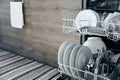 Opened dishwasher machine at kitchen with clean utensil, white plates Royalty Free Stock Photo