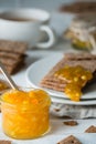 Closeup of orange jam in glass jar and brown rye crisp bread Swedish crackers with spread jam on them