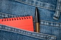 Orange notebook and black pen in blue jeans pocket