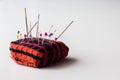 Closeup of an orange and pink  pin cushion with colorful pushpins and needles on a white surface Royalty Free Stock Photo