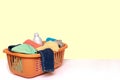 Closeup of a orange wash basket with colorful dirty clothes and a white detergent bottle on a bright table against light yellow