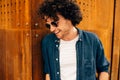 Closeup outdoors portrait of happy man standing outside, waiting his friends. Young male student with curly hair wears sunglasses Royalty Free Stock Photo