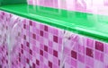 Overflowing water of vibrant green and magenta pink tiled swimming pool spillway