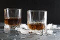 Closeup of pair of ol fashioned glasses.Brandy and pieces of ice on gray table against dark wall Royalty Free Stock Photo