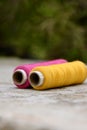 Closeup the pair of pink yellow thread reels over out of focus grey green background Royalty Free Stock Photo