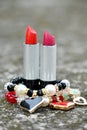 closeup the pair of red,pink color lipstick silver black tube with red white plastic beads bracelet soft focus natural grey brown Royalty Free Stock Photo