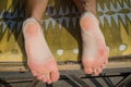 Closeup of pair of sandy female feet on beach lounger with geometrical pattern outdoors on sunny day Royalty Free Stock Photo