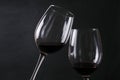 Closeup of pair of wineglasses, red wine against black background. Cheers concept