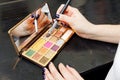 Closeup palette of an eye shadows and womans hand with brush.