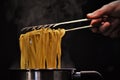 Closeup of a person holding hot pasta with a spaghetti tong with a dark blurry background Royalty Free Stock Photo