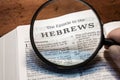 Closeup of a person holding a magnifier and reading the book of Hebrews from the New Testament