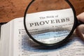 Closeup of a person holding a magnifier and reading the book of Proverbs from the New Testament Royalty Free Stock Photo