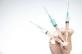 Closeup of a person with a latex glove holding three needle syringes against a white background