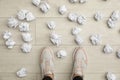 Closeup of person`s feet surrounded by crumpled paper on floor, top view.