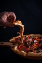 Closeup of a person taking a slice of a freshly baked delicious pizza on a wooden tray