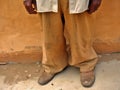 A closeup of a person wearing worn clothes and shoes that are too big the emptiness of the pockets a sign of poverty