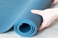 Closeup of a person's hand unfolding a blue yoga mat on a floor