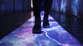 A closeup of a persons feet as they walk along a dark hallway and activate projected images and animations to guide them