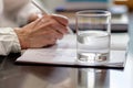 closeup of a persons hand taking notes with a halffull water glass Royalty Free Stock Photo