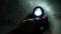 A closeup of a persons sweating palms gripping onto a flashlight as they cautiously navigate through a pitchblack tunnel