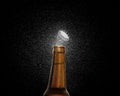 Closeup photo of an amber beer bottle splashing beer drops on a black background. Beer cap flying on top of the bottle Royalty Free Stock Photo