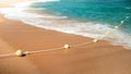 Closeup photo of beatiful sandy sea beach and waves rolling over life buoys line on the rope Royalty Free Stock Photo