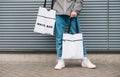 Closeup photo of bottom of stylish man in casual clothes holding 2 white eco bags in his hand. Advertising stylish reusable eco