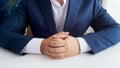 Closeup image of businessman in blue suit with folded hands sitting behind white wooden office desk Royalty Free Stock Photo