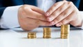 Closeup image of businessman sitting behind office desk with three stacks of golden coins Royalty Free Stock Photo