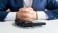 Closeup photo of businessman sitting in front of revolver lying on stack of money