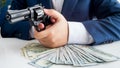 Closeup image of businessman with stack of money aiming with revolver