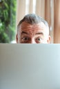 Closeup photo of cheerful mature businessman working with laptop computer and peeking out from behind monitor, free copy