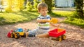 Closeup image of cute little boy playing on the palyground with toys. Child having fun with truck, excavator and trailer