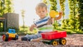 Closeup image of cute little boy playing on the palyground with toys. Child having fun with truck, excavator and trailer