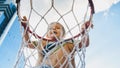 Closeup image of cute smiling toddler boy holding and hanging on basketball ring on sportrs playground at city Royalty Free Stock Photo