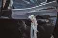 Closeup photo of decorater car`s door with white roses and silk bow.