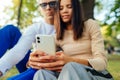 Closeup photo of a female hands holding the smartphone and using the device. Young couple is chatting in the park. Focus on a Royalty Free Stock Photo
