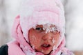 Closeup photo of female kid with sad face covered with snow and about to cry wearing pink winter clothes in forest Royalty Free Stock Photo