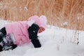 Closeup photo of female Russian kid crawling in snow and looking at snow wearing pink winter clothes in forest Royalty Free Stock Photo