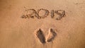 Closeup image of footprints and 2019 numbers written on wet sand at the sea beach. Concept of New Year, Christmas and Royalty Free Stock Photo