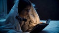 Closeup image of girl lying in bed and reading book a tnight Royalty Free Stock Photo