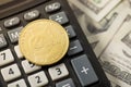 Closeup photo of gold coin with dogecoin symbol on calculator and hundred dollar banknotes