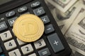Closeup photo of gold coin with dogecoin symbol on calculator and hundred dollar bills