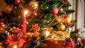 Closeup image of golden gift box and burning candle against beautiful Christmas tree Royalty Free Stock Photo