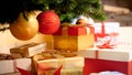 Closeup image of golden and red baubles hanging on Christmas tree over big heap of gifts and presents in boxes at living