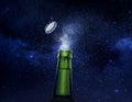 Closeup photo of an green beer bottle splashing beer drops on a stars background. Beer cap flying on top of the bottle Royalty Free Stock Photo