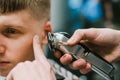 Closeup photo, hairdresser hand with clipper cuts hair of young man. Creating stylish men`s haircut in barber shop. Background. Royalty Free Stock Photo