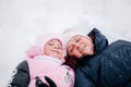 Closeup photo of kid lying in snow with mother and both looking into camera wearing pink winter clothes in forest Royalty Free Stock Photo