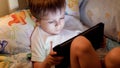 Closeup photo of little boy going to sleep and browsing internet on digital tablet computer